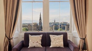 A room with a large window, a purple sofa, and two pillows. - Fraser Suites Edinburgh (Edinburgh)