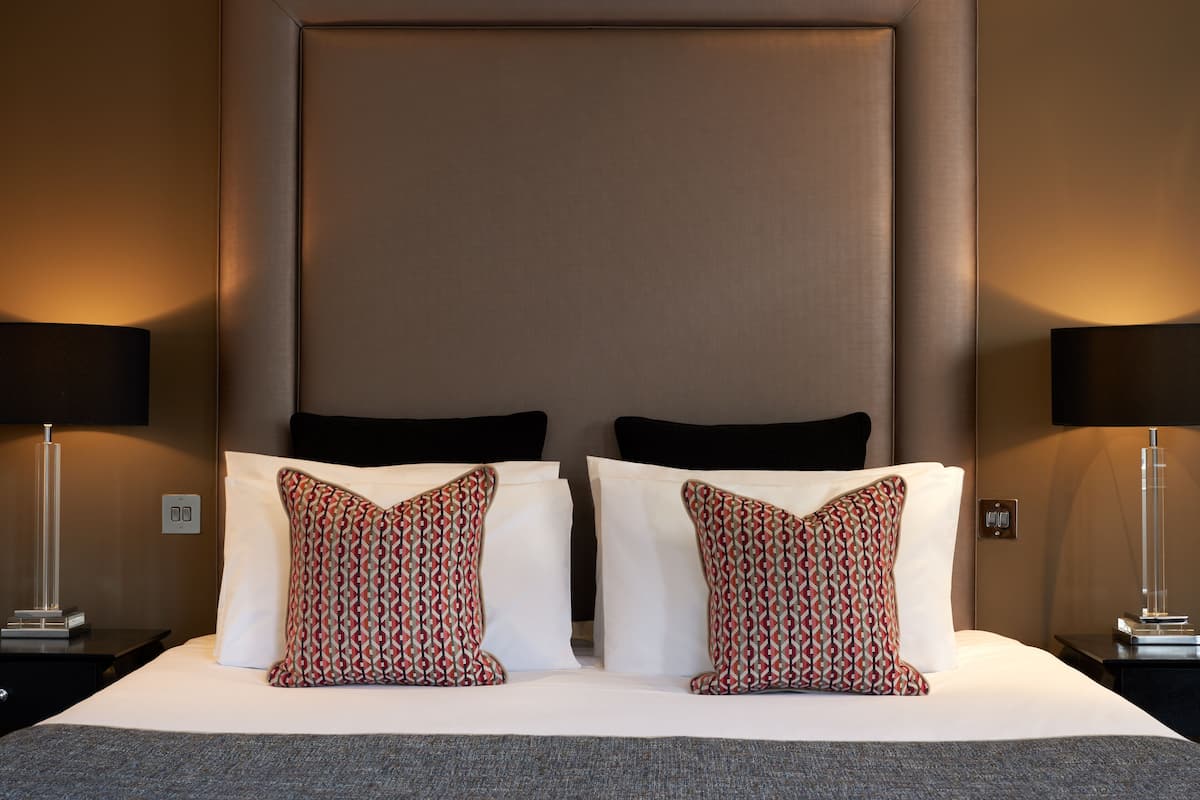 A hotel room with a large bed, two patterned pillows, black headboard, and two bedside lamps.