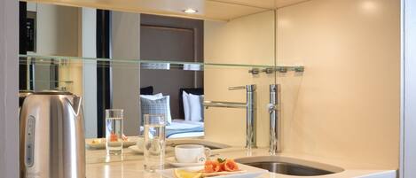 Une cuisine moderne avec une bouilloire, un verre d’eau et une assiette de nourriture sur le plan de travail.