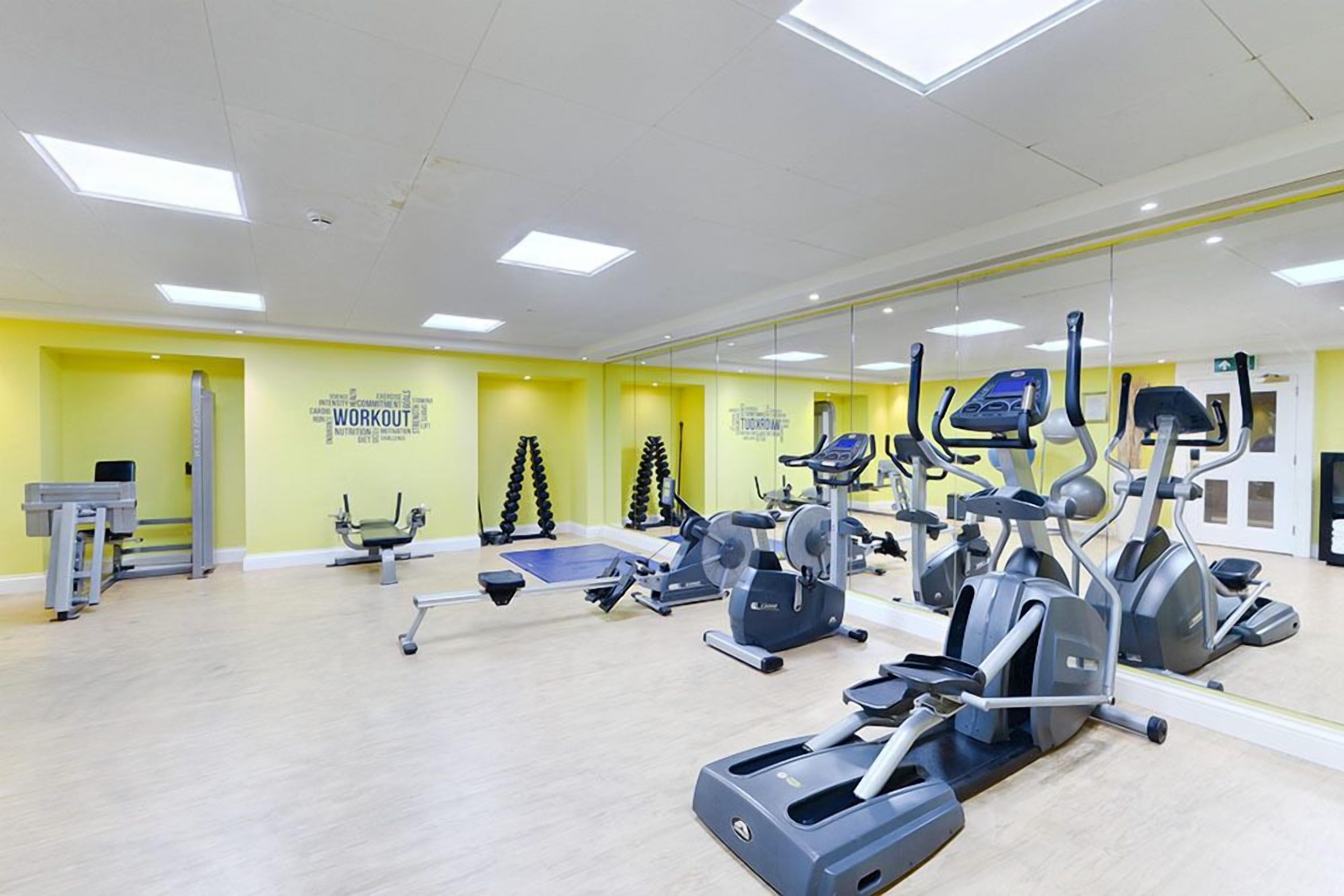 Une salle de sport équipée de machines de cardio, de machines de musculation et dotée d’un mur entièrement recouvert de miroirs.
