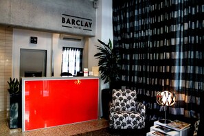 A reception area with a red desk, a black and white patterned chair, a potted plant, and a wall with a checkered pattern.