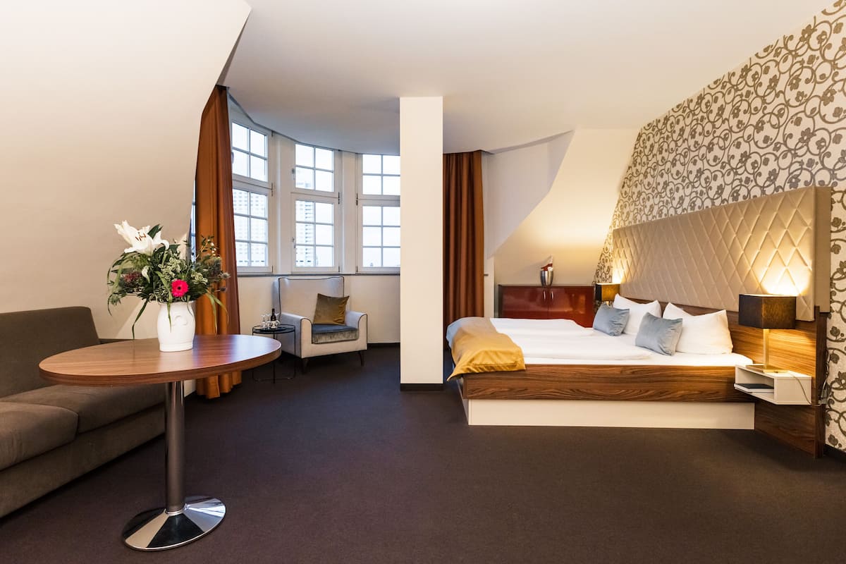 A hotel room with a bed, a round table, a sofa, a chair, and a window with curtains.