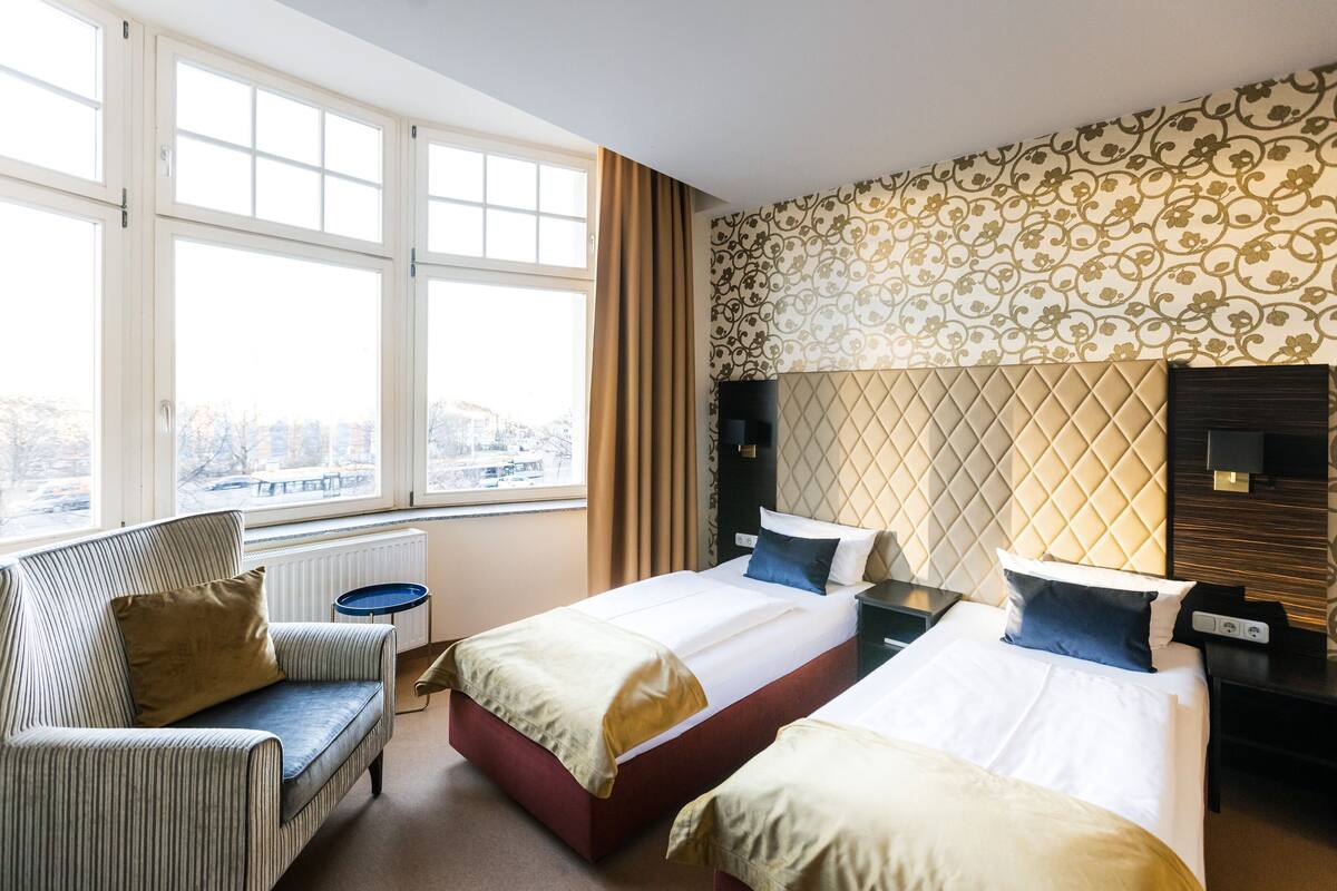 A hotel room with two beds, a sofa, a small table, and a view of the city.