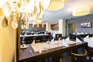 Een restaurant met meerdere eettafels, gedekt met wit servies, een kroonluchter en een stenen muur met een televisie.