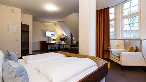 A hotel room with a large bed, a desk with a chair, a television, and a window with curtains. - Hotel Royal International (Leipzig)