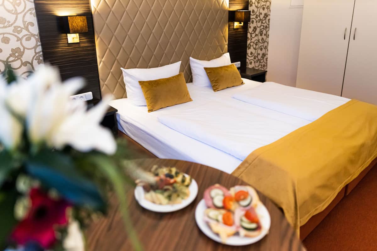 A hotel room with a large bed, two pillows, a nightstand with a plate of food, and a decorative wall panel.