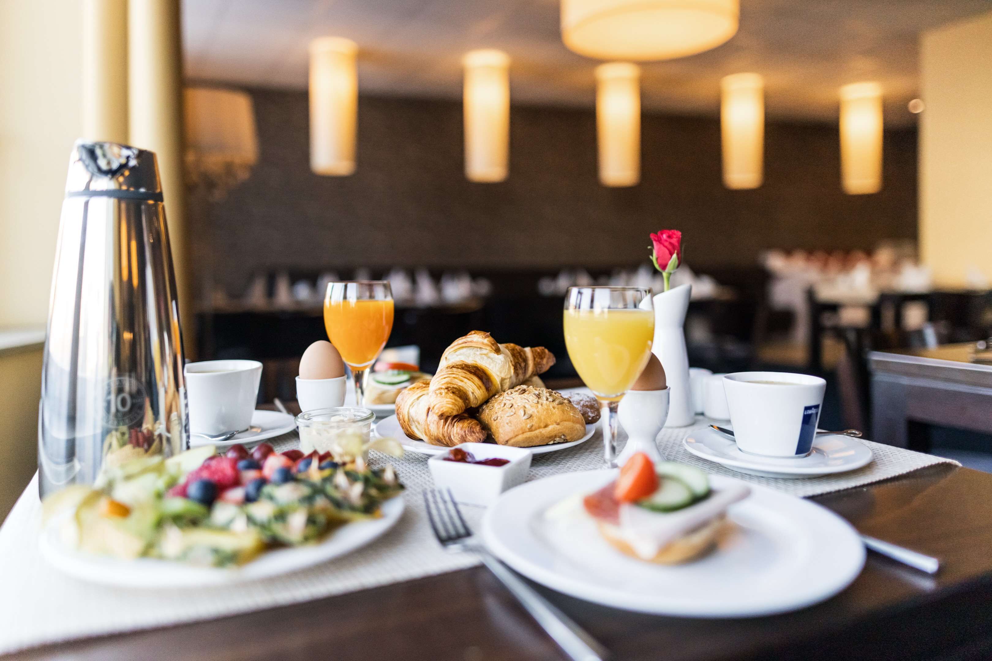 Ett frukostbord med croissanter, frukt, juice och kaffekoppar, placerat i en restaurangmiljö.