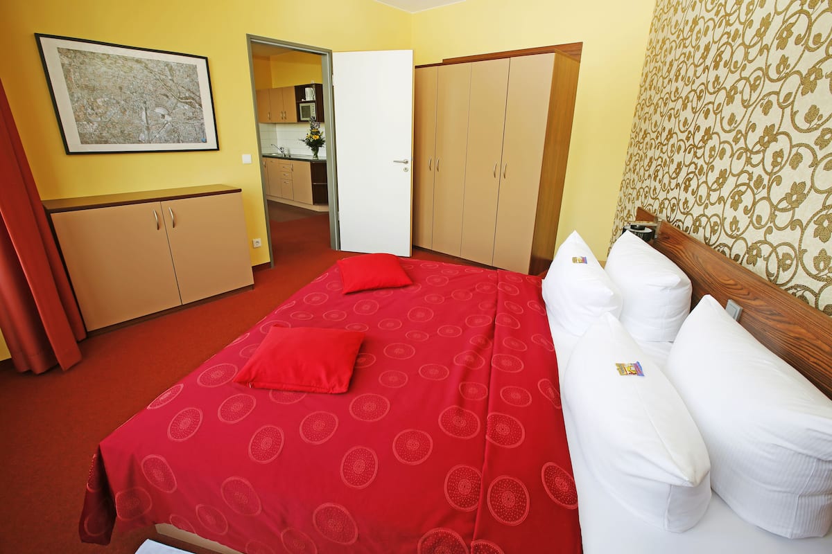 A hotel room with a red patterned bedspread, a wooden headboard, and a large window.