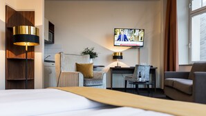 A hotel room with a large bed, a desk with a chair, a television mounted on the wall, and a window with curtains. - Hotel Royal International (Leipzig)