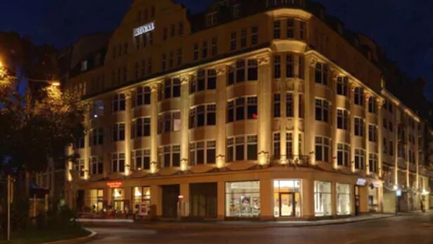 A large, multi-story hotel with a classic architectural style, featuring a prominent corner entrance and illuminated windows. - Hotel Royal International (Leipzig)