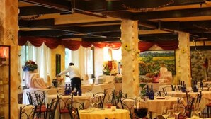 Un restaurant amb diverses taules preparades per dinar, un xef preparant menjar i una vista exterior panoràmica.