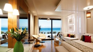 A modern living room with a large window overlooking the sea, a sofa, a dining area, and a view of the ocean. - Amus Hotel & Spa (Rhodes)