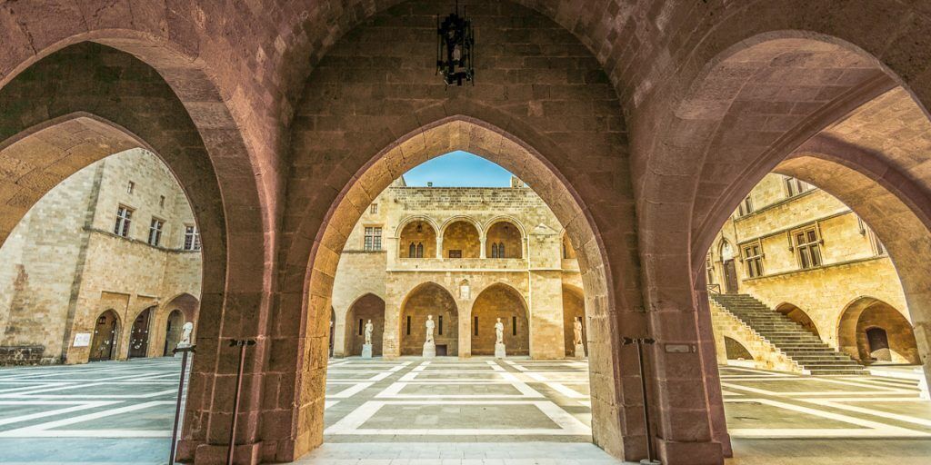 A courtyard with arches, a central courtyard, and a building with multiple windows in the background.