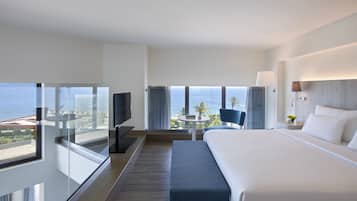 Een hotelkamer met een groot bed, een televisie, een klein tafeltje met een stoel, en een balkon met uitzicht op zee.