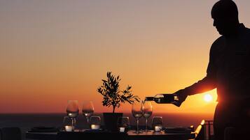 Mesa preparada para una comida, con copas de vino y una planta, con vista a la puesta de sol.