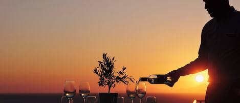 A table set for a meal with wine glasses and a plant, overlooking a sunset.