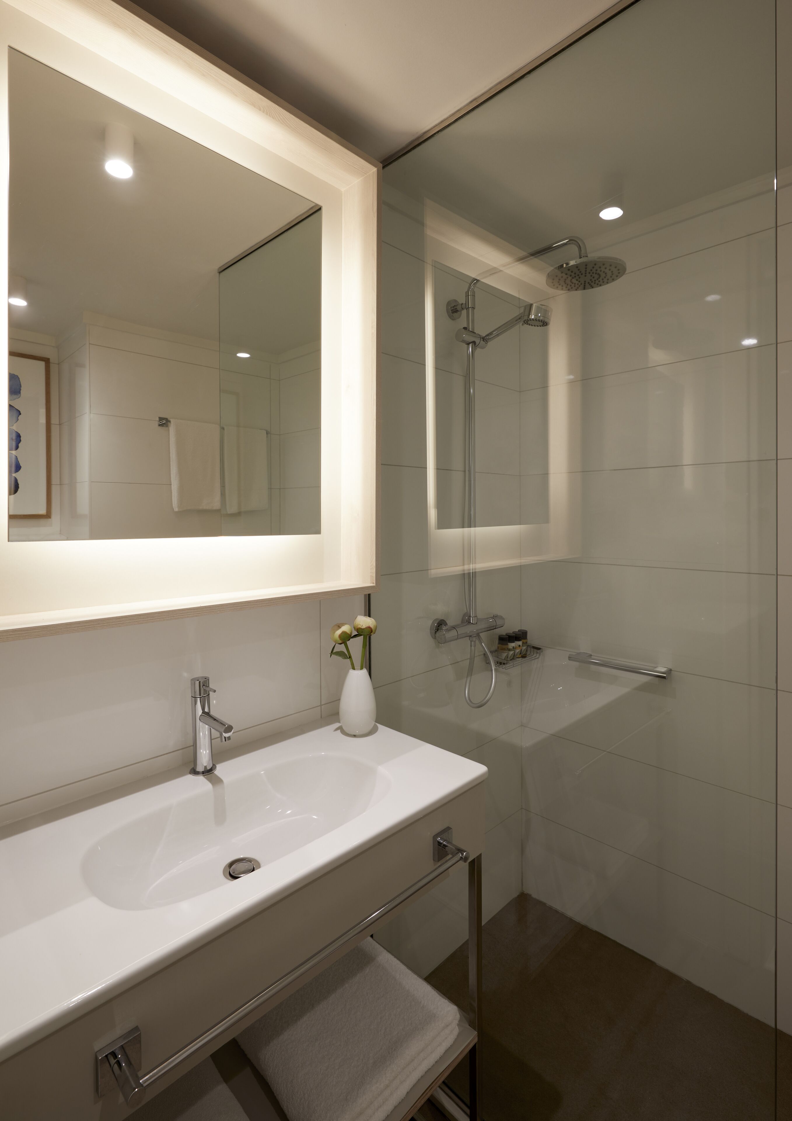 A modern bathroom with a large mirror, a white sink, a glass-enclosed shower, and a towel rack.
