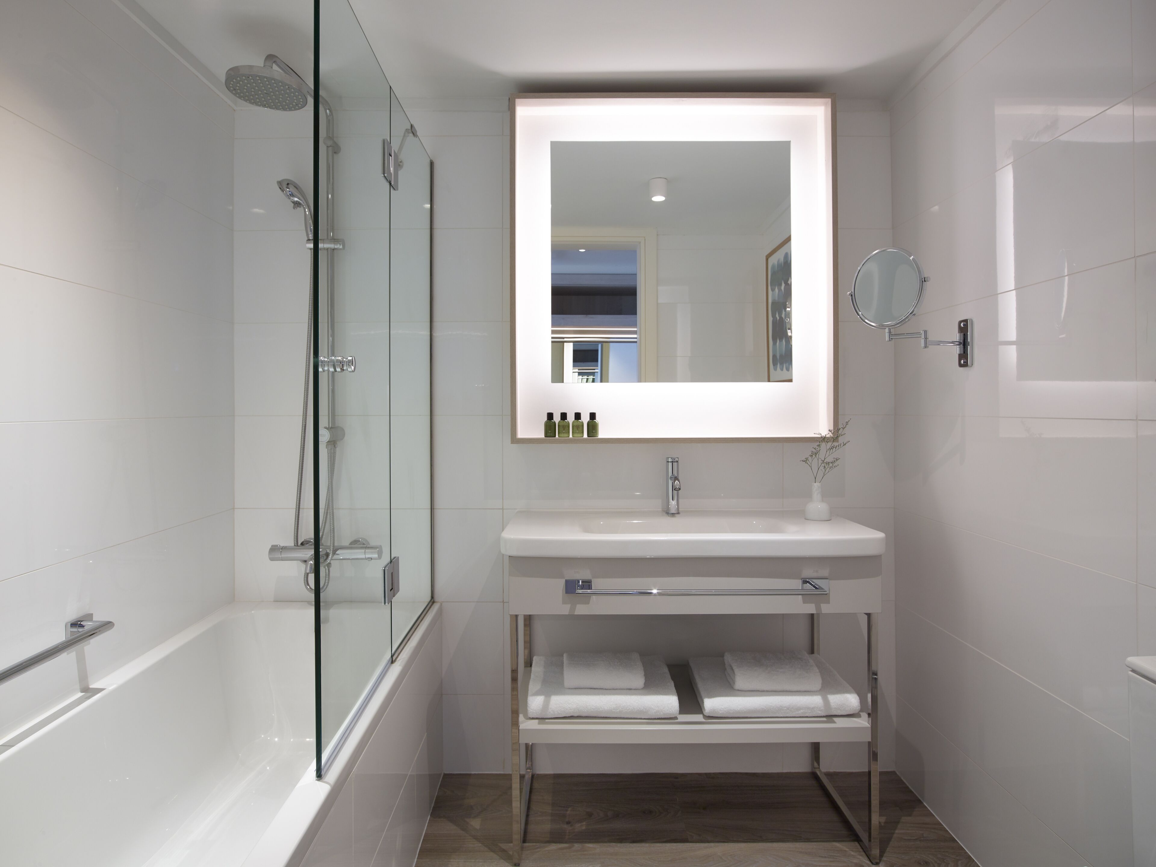 A modern bathroom with a glass-enclosed shower, a white sink with a mirror above it, and a shelf with towels.
