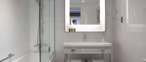 A modern bathroom with a glass-enclosed shower, a white sink with a mirror above it, and a shelf with towels.