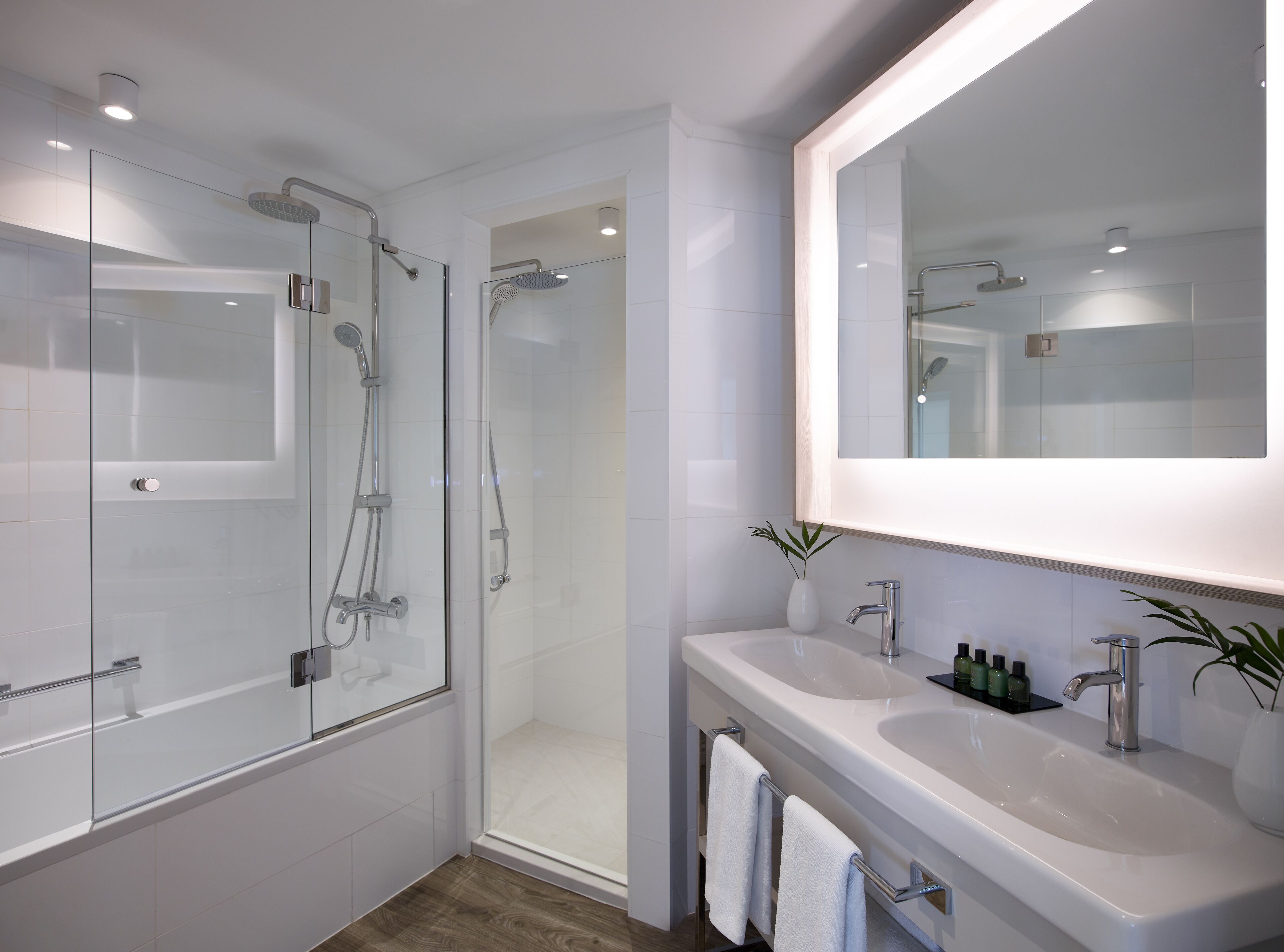 Un baño moderno con ducha envuelta en vidrio, un espejo grande y un lavamanos con dos lavabos.