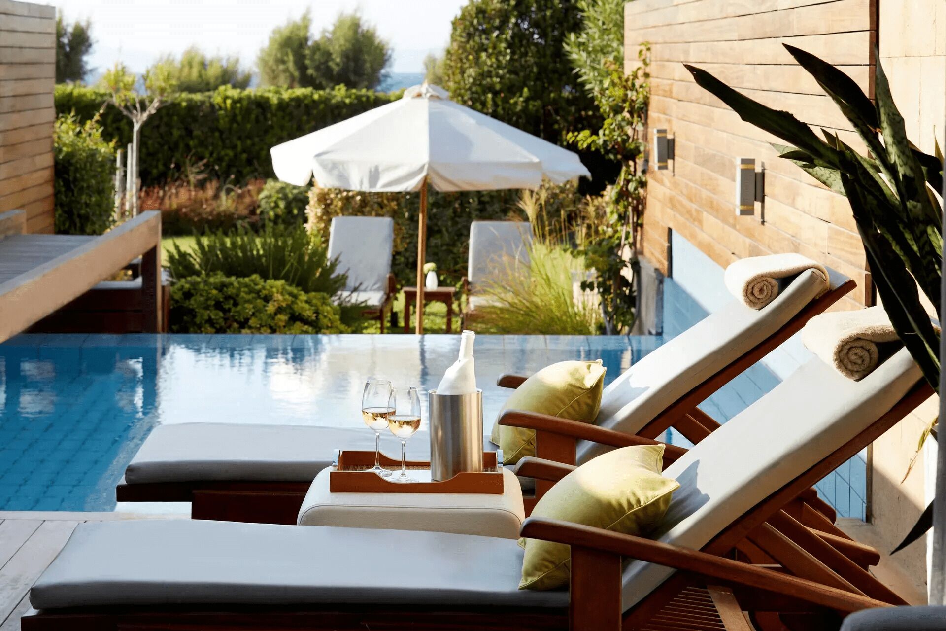 Zona de piscina con sillones de descanso, una sombrilla y una botella de champán.
