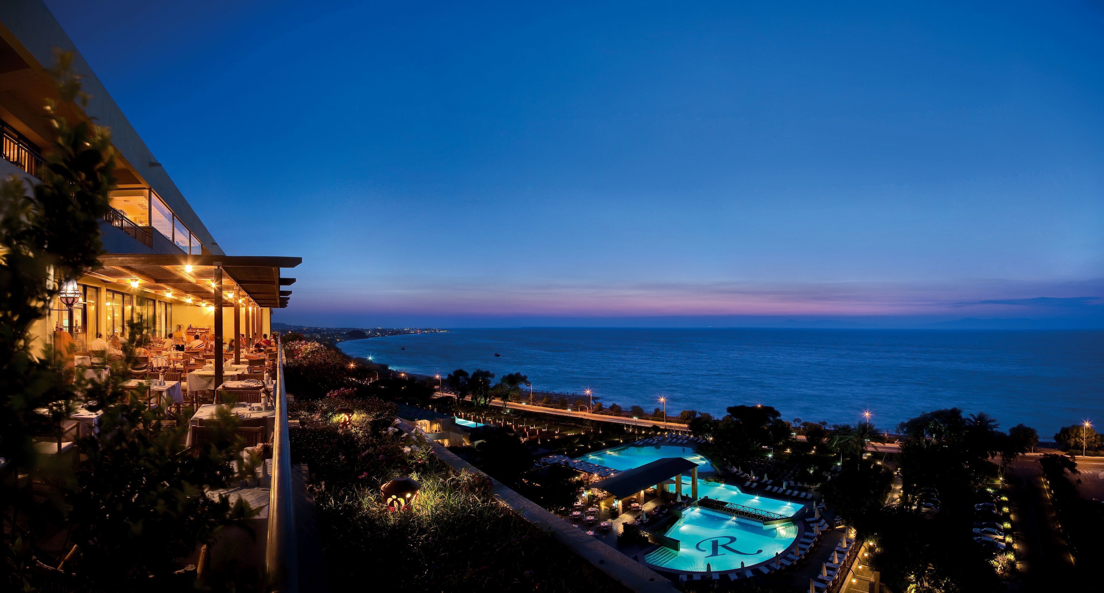 Un resort con area piscina, posti a sedere all'aperto e vista sull'oceano al tramonto.