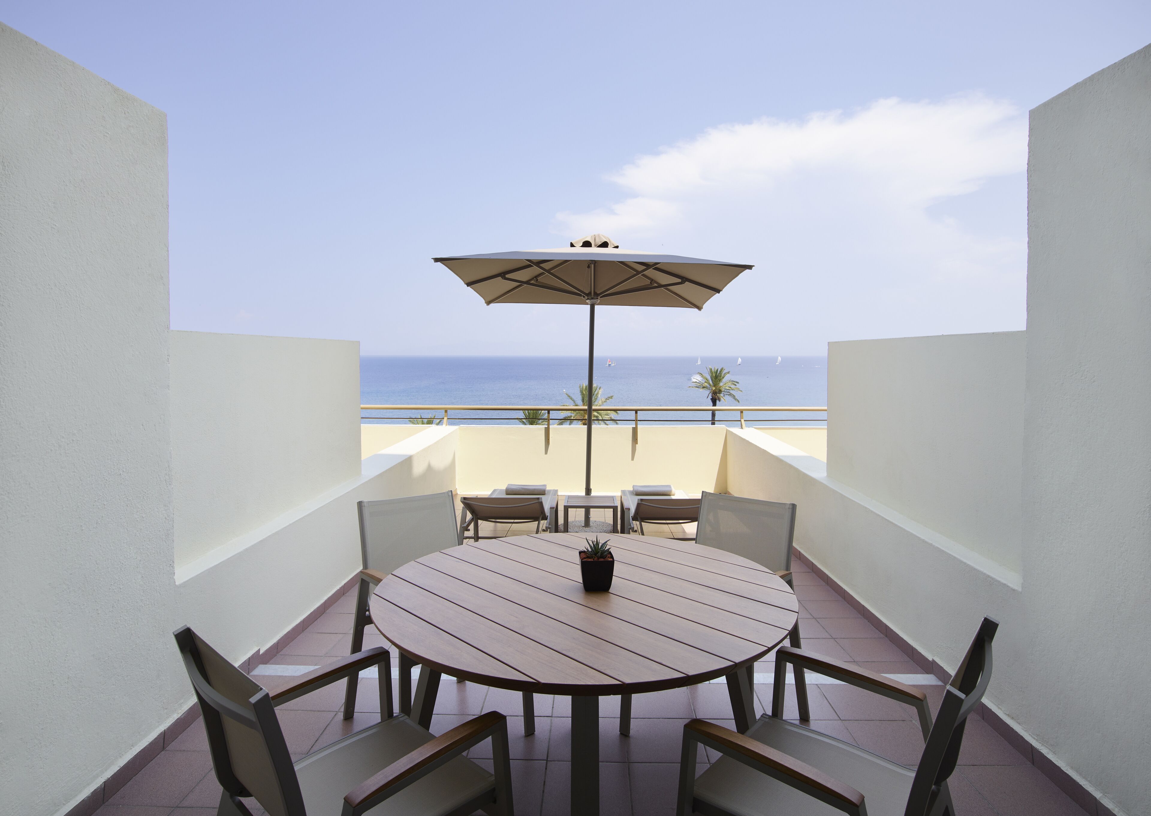 A round table with chairs and an umbrella on a balcony overlooking the sea.