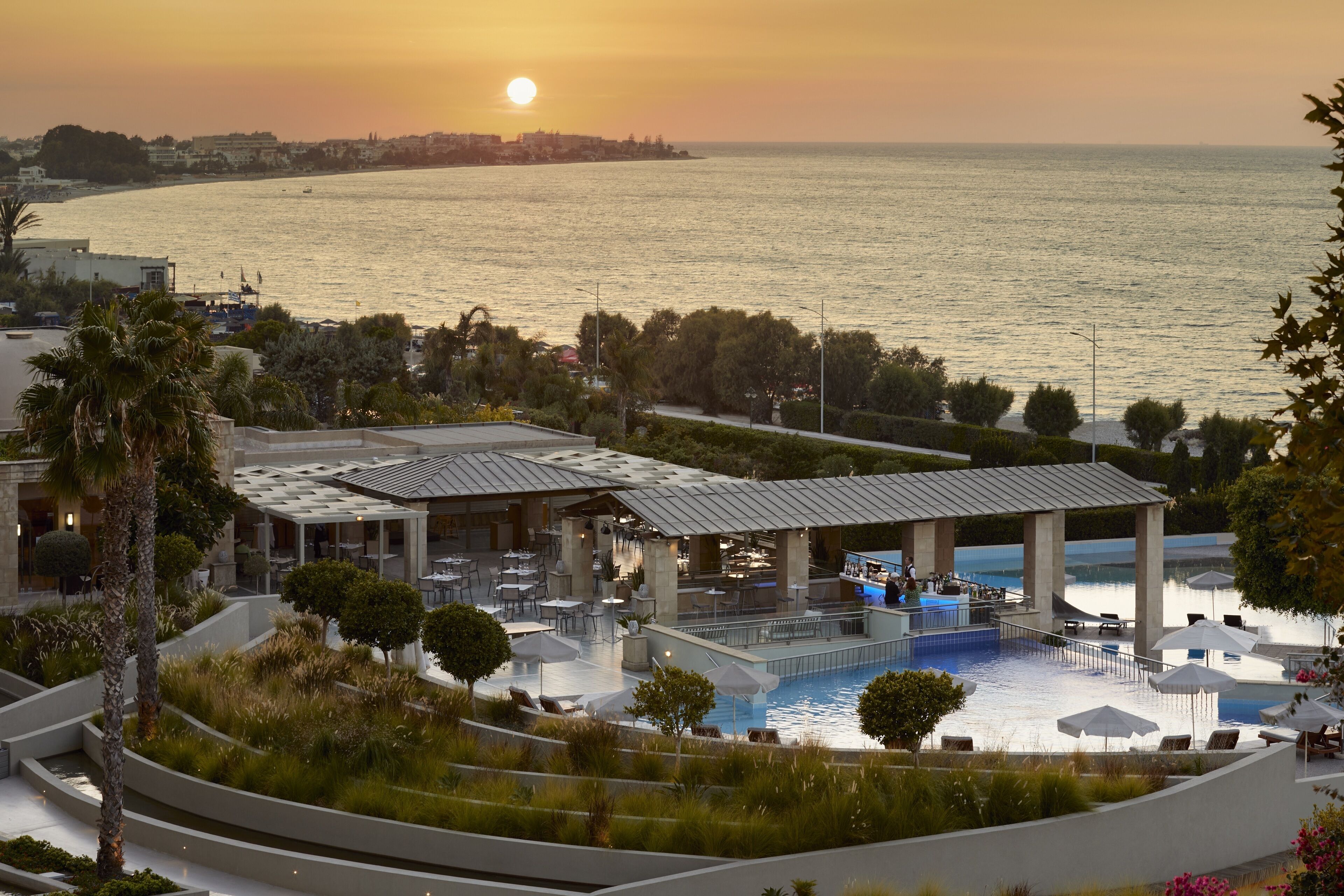 Un resort con piscina, mobiliario exterior y vistas al mar al atardecer.