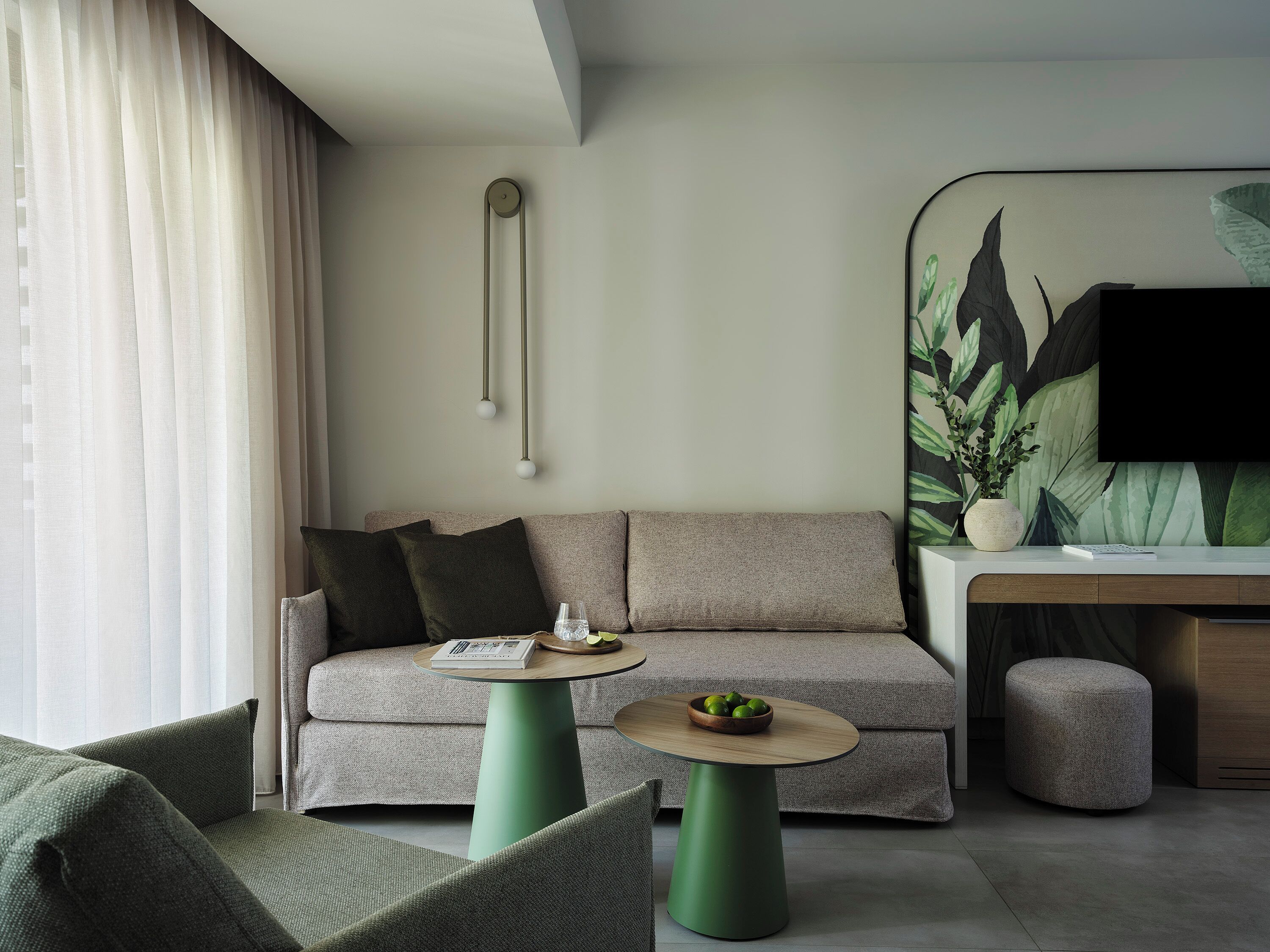Un salon moderne avec un canapé, une table ronde sur laquelle se trouve un saladier de fruits, un pouf vert et un téléviseur fixé au mur.