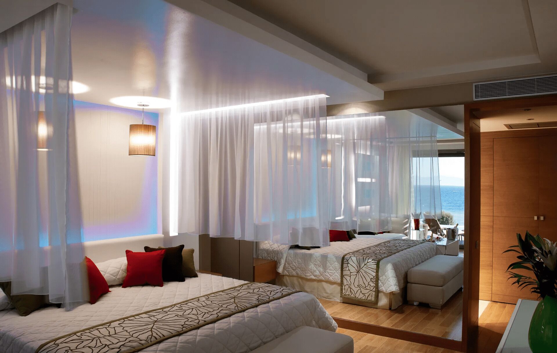 A hotel room with two beds, a large mirror reflecting the room, a view of the sea, and a wooden wardrobe.