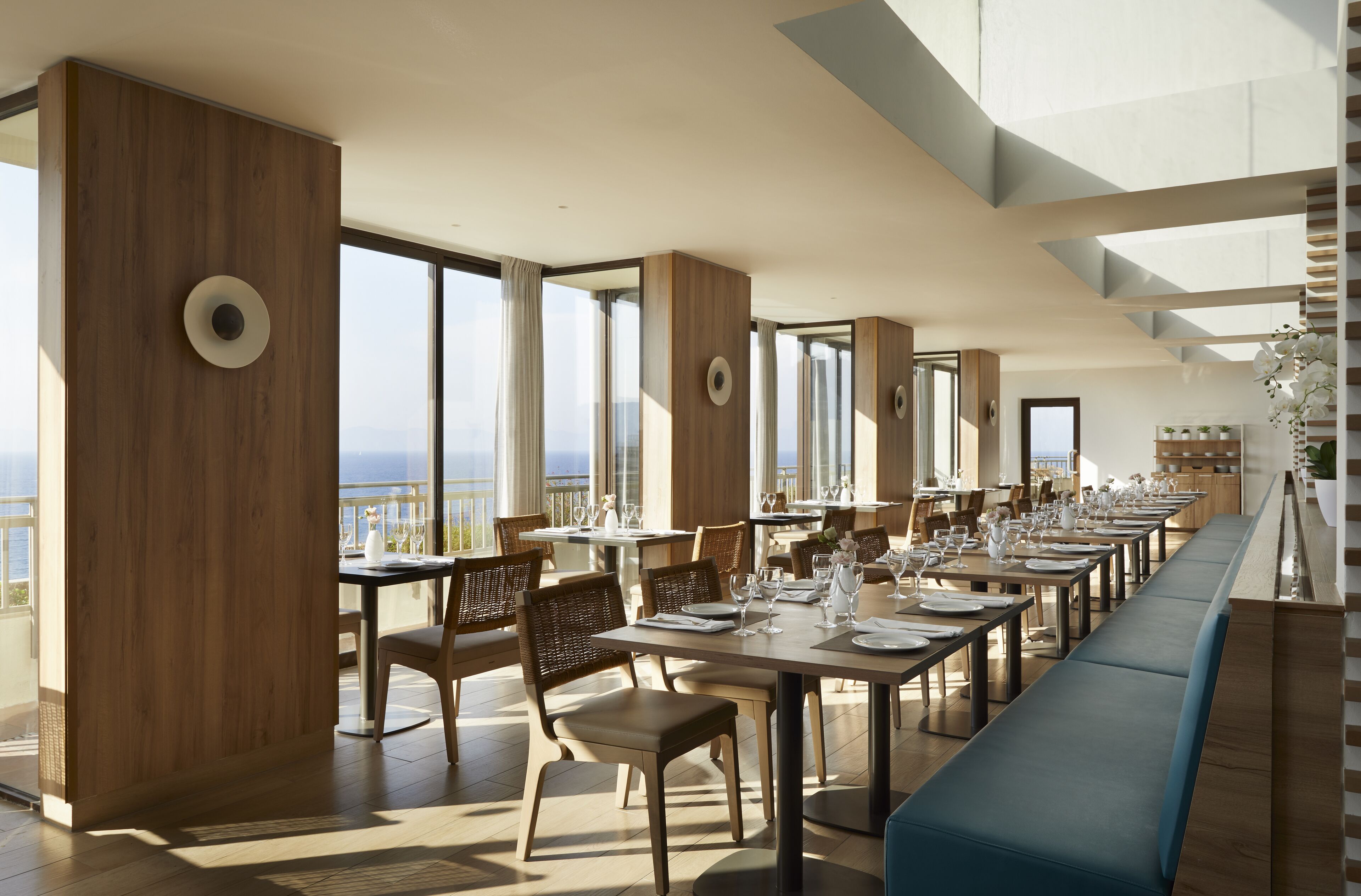 A modern dining area with high ceilings, large windows, and a long bench.