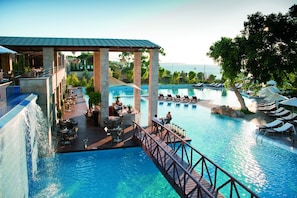 A resort pool area with a wooden deck, lounge chairs, and a view of the sea.