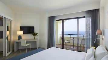 Habitación de hotel con cama, escritorio, silla, televisor y balcón con vista al océano.