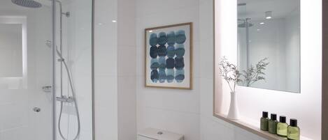 A modern bathroom with a glass-enclosed shower, a toilet, a sink with a mirror, and a framed abstract painting on the wall.