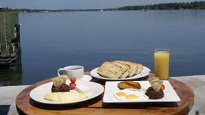 Una mesa de desayuno con platos de comida y un vaso de jugo de naranja, con vista a un lago tranquilo.