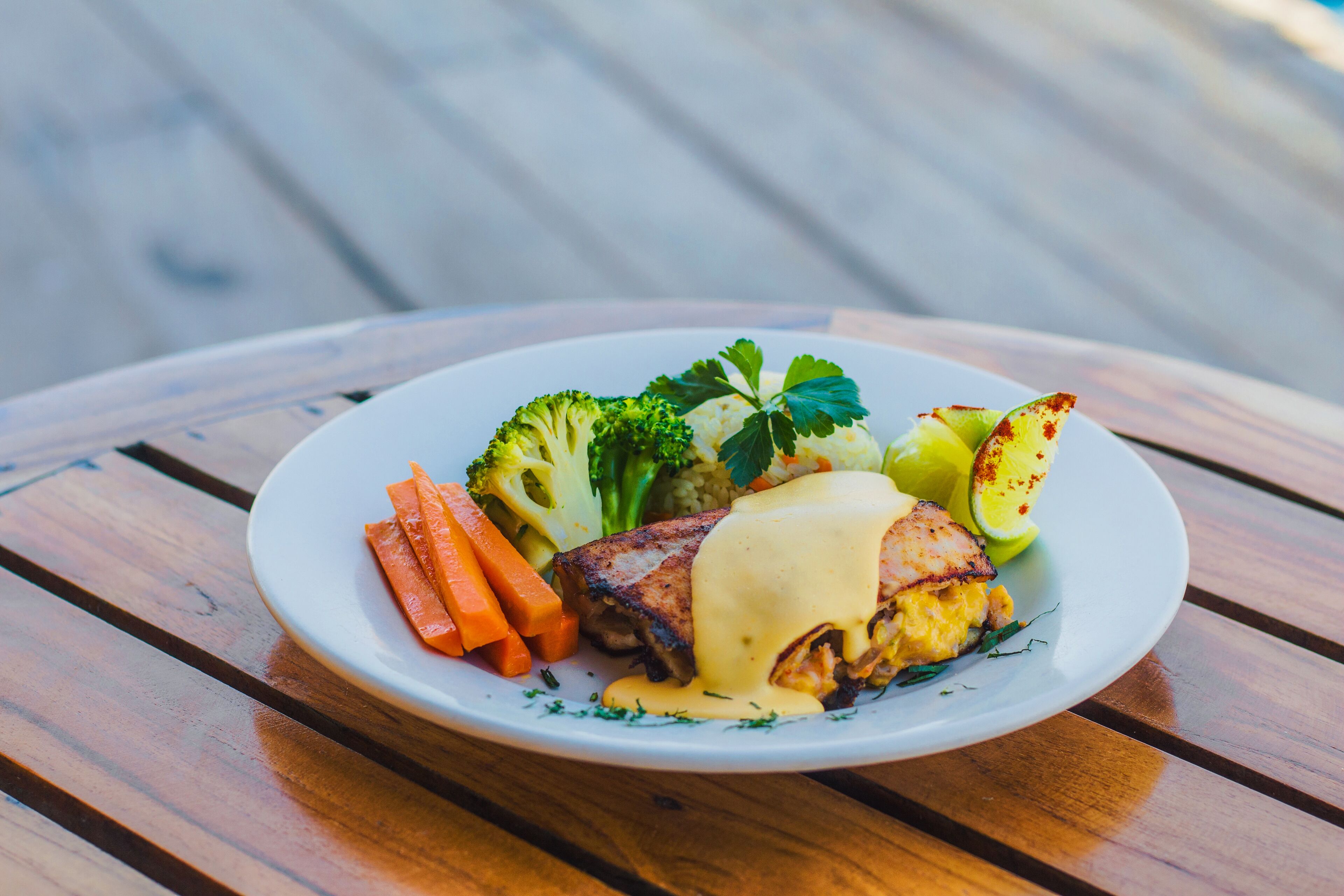 Une assiette de nourriture comprenant un steak, des légumes et une sauce, posée sur une table en bois.