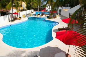 A swimming pool with a curved edge, surrounded by palm trees and red umbrellas. - Hotel Bahia Del Sol (La Herradura)