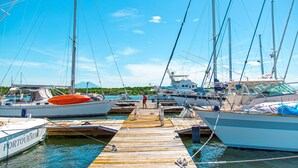 Un puerto deportivo con varias embarcaciones amarradas, un muelle de madera y una persona de pie sobre el muelle.