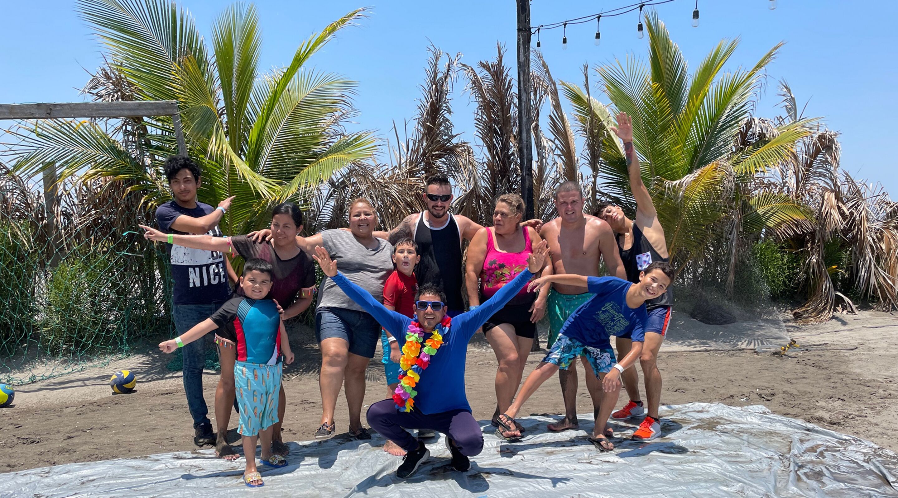 A group of people posing on a beach with palm trees and a clear sky in the background.