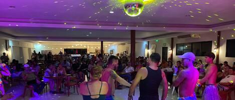Un amplio espacio interior con una bola de discoteca, mesas y sillas dispuestas para un evento social.