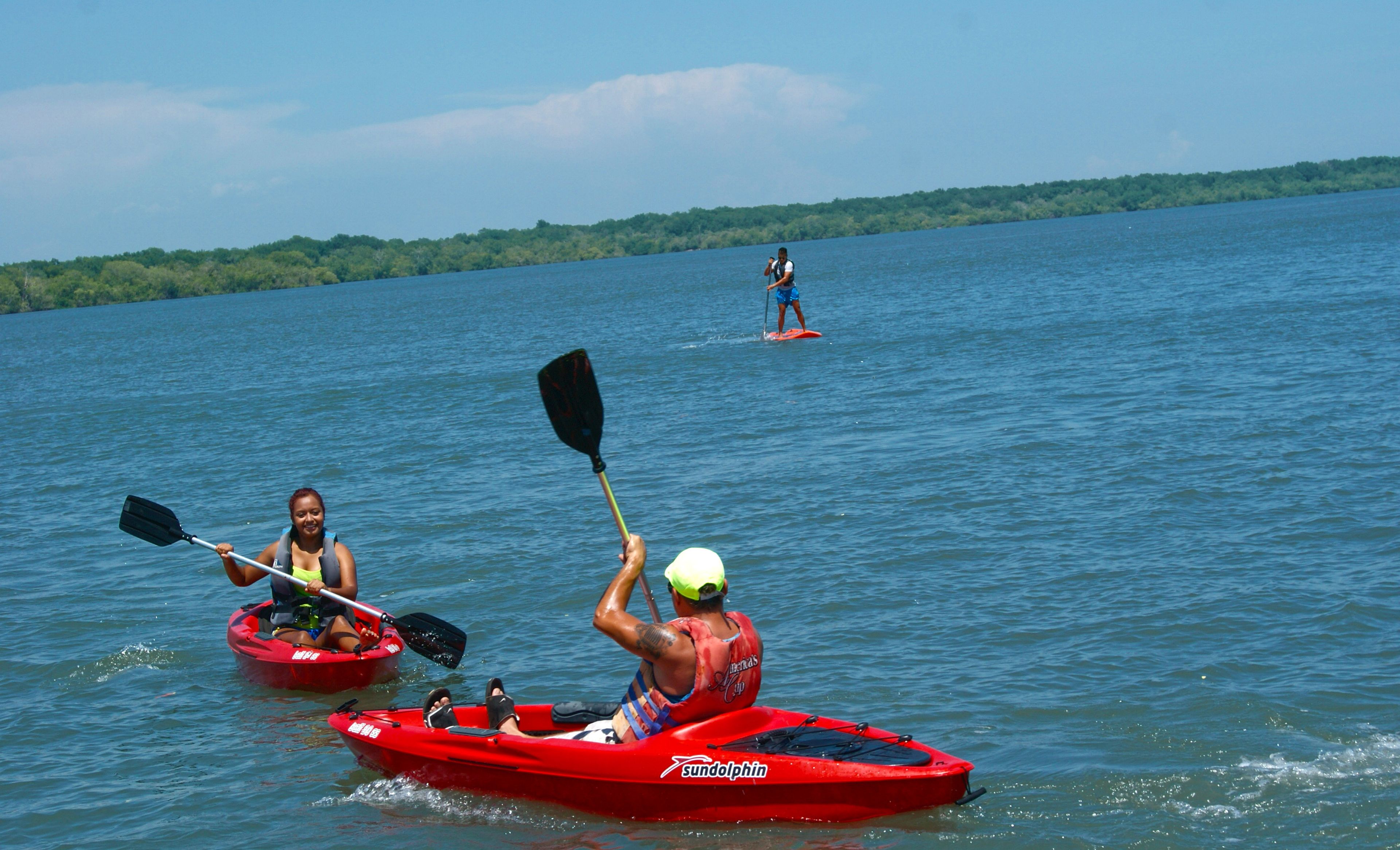 Dos personas en kayak en un lago tranquilo, con una orilla lejana.