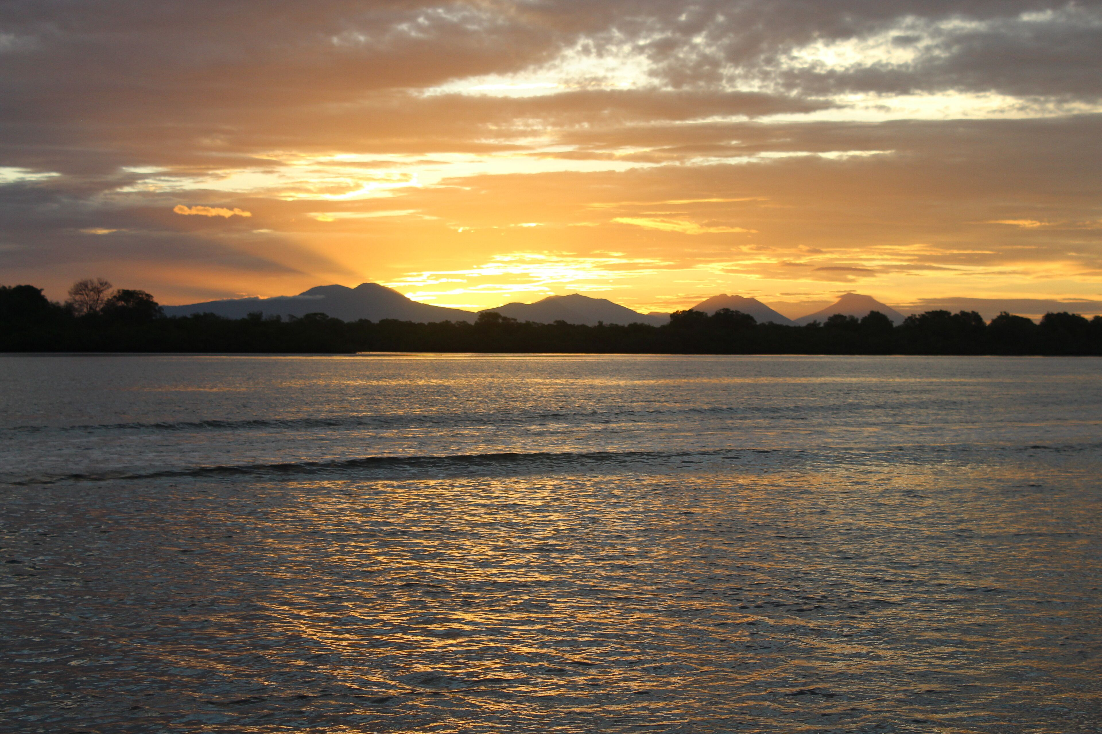Un coucher de soleil sur une étendue d'eau calme, avec des montagnes en arrière-plan.