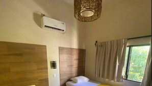 Habitación de hotel con dos camas, una ventana con cortinas, un equipo de aire acondicionado y una lámpara fijada a la pared.