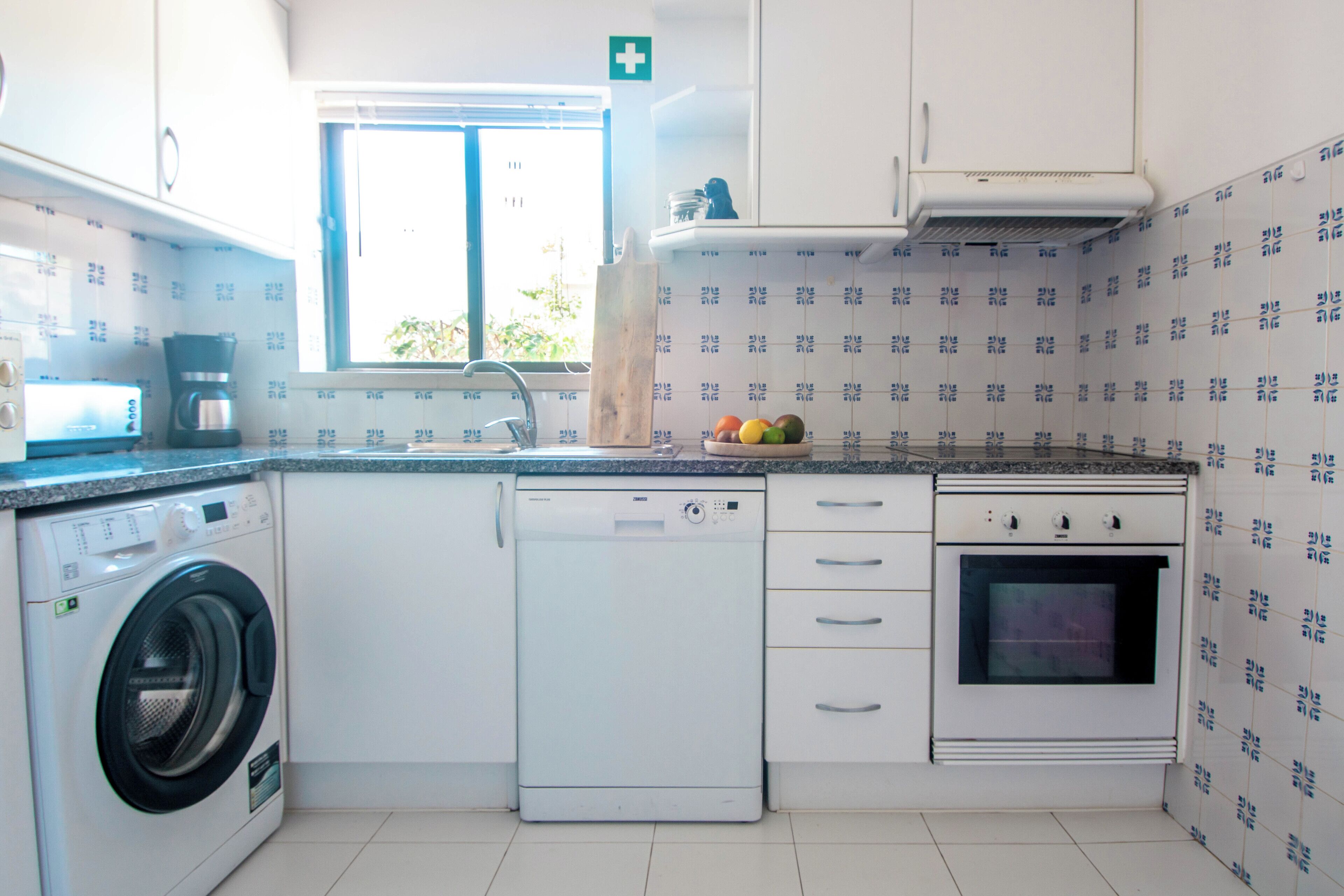 Una cocina compacta equipada con lavadora, cafetera, lavaplatos y estufa.