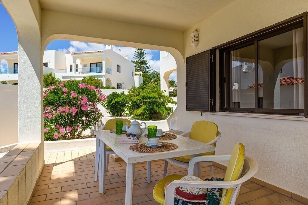 A patio with a table set for two, surrounded by yellow chairs, and a view of neighboring buildings.