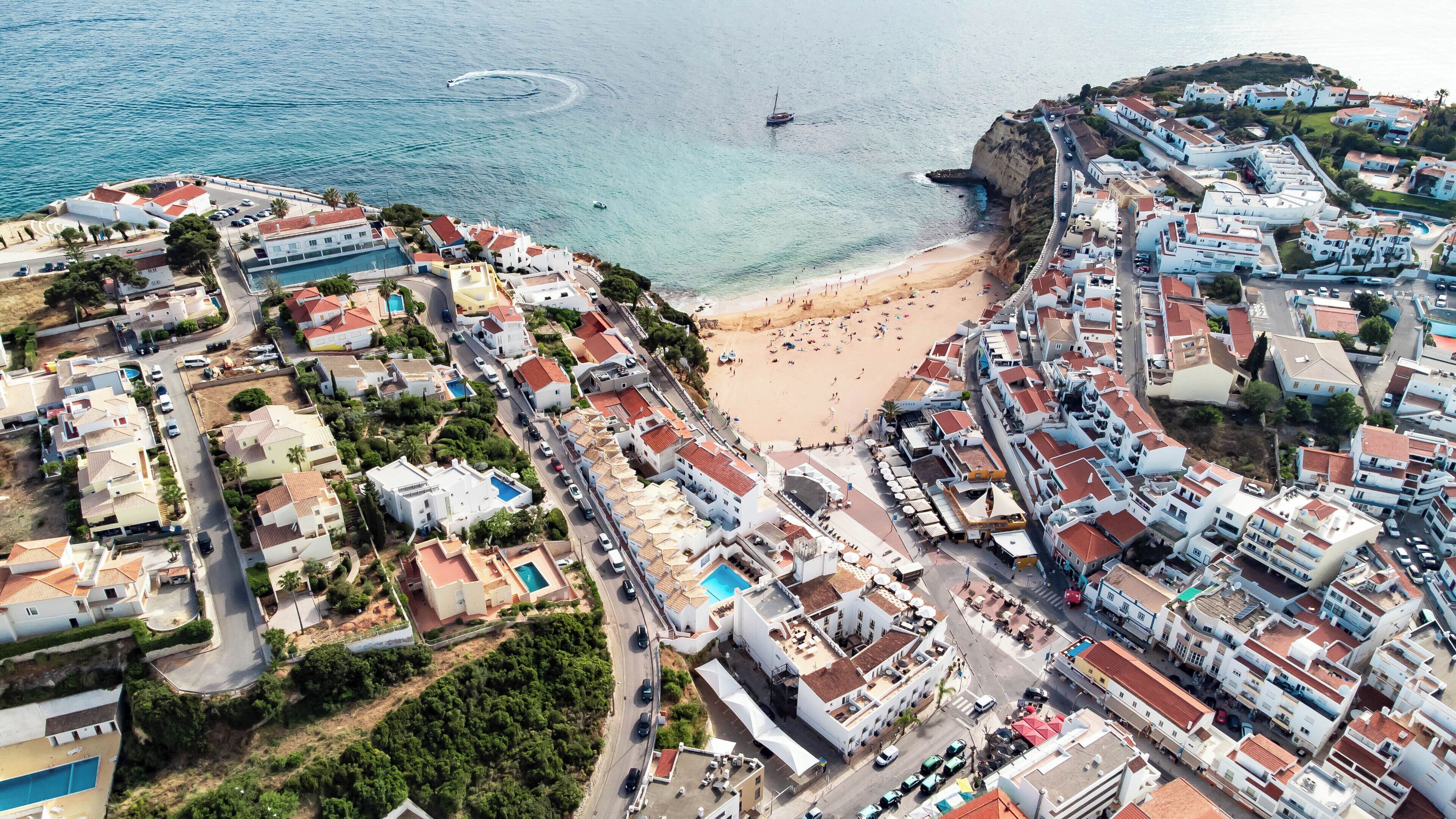 Vista aérea de un pueblo costero con playa, edificios residenciales y un puerto deportivo.
