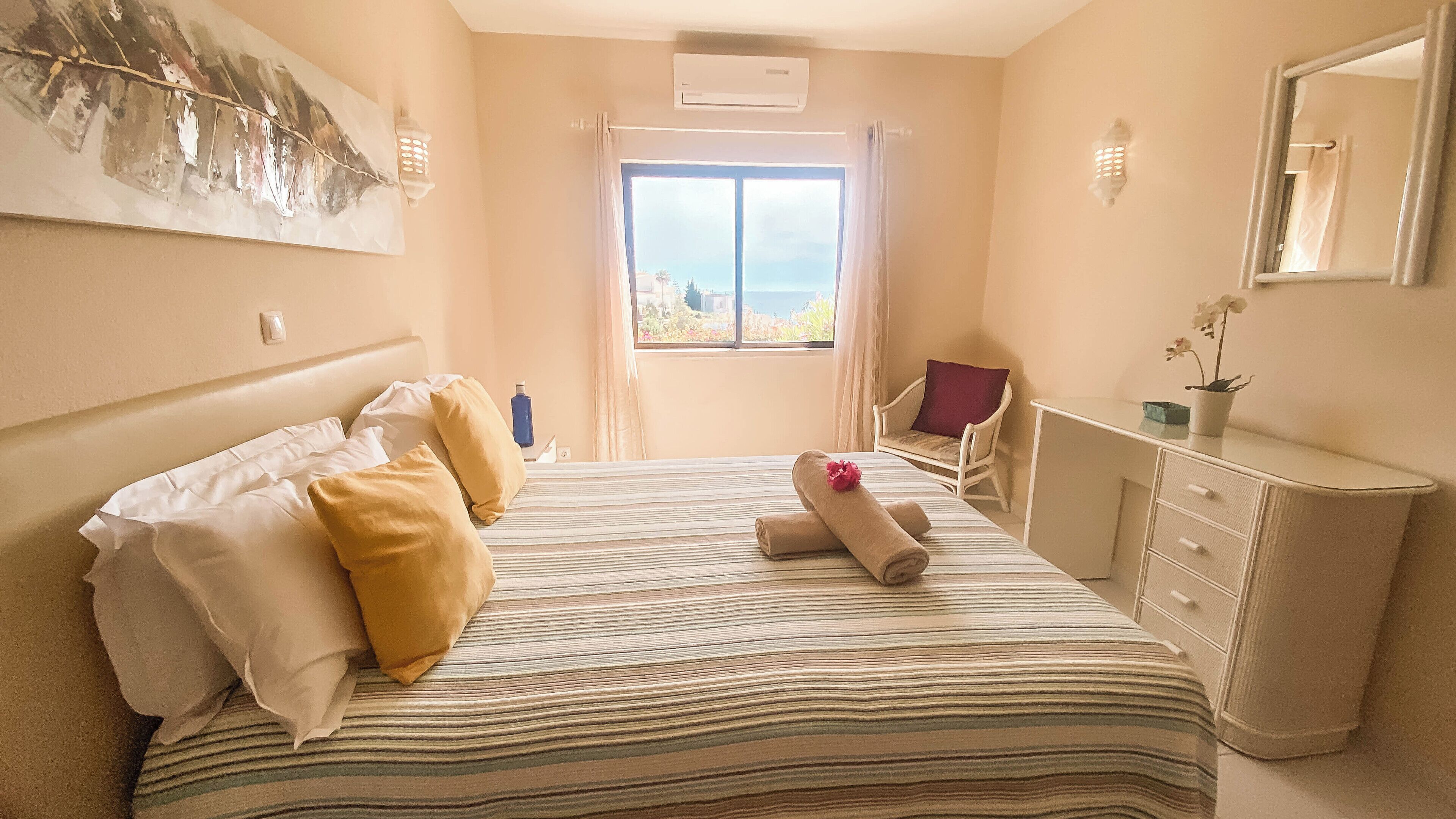 A hotel room with a bed, a desk, a chair, a window with a view, and a painting on the wall.