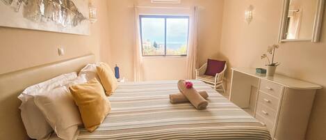 A hotel room with a bed, a desk, a chair, a window with a view, and a painting on the wall.