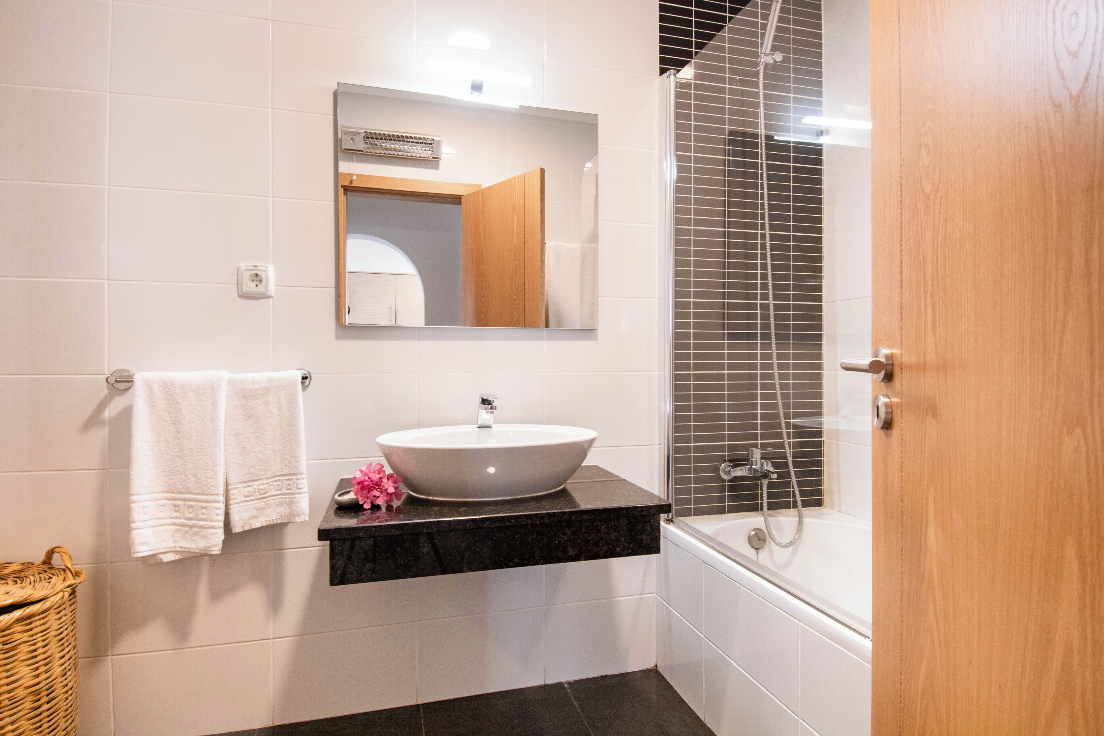 A bathroom with a white sink, a mirror, a shower, and a wooden door.