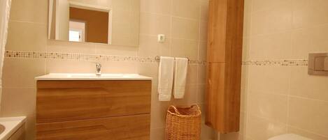 Un baño con tocador de madera, espejo, lavamanos, inodoro y cesta de mimbre.